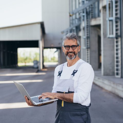 worker using laptop , grain silo in blurred background Supply chain medewerker met laptop