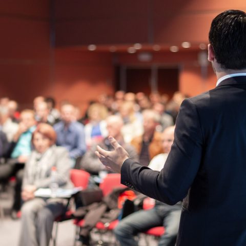 Public speaker giving talk at business event. Speaker giving a talk on corporate business conference. Unrecognizable people in audience at conference hall. Business and Entrepreneurship event.